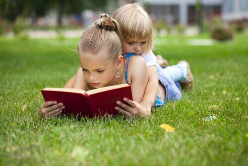 Petite-fille-lisant-un-livre-sur-l'herbe-avec-sa-soeur
