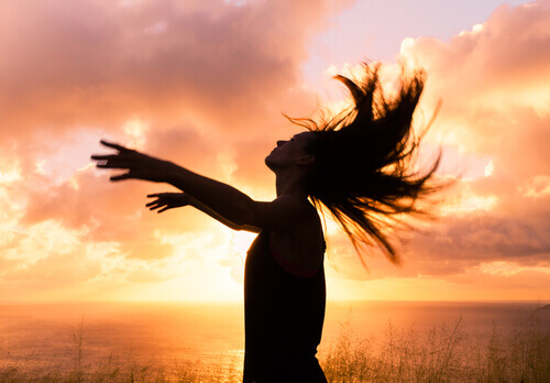 femme-avec-les-bras-ouverts-coucher-de-soleil