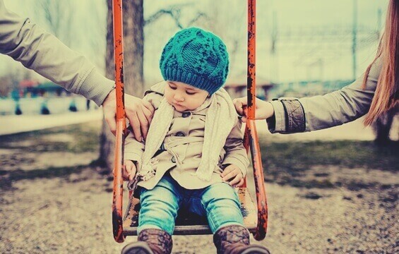 enfant sur une balançoire avec les bras de ses parents sur les côtés