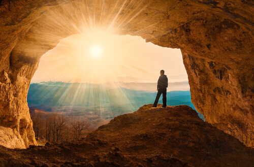 homme dans une grotte face au soleil