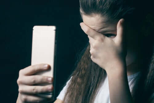 Une jeune fille qui se cache le visage en tenant son portable