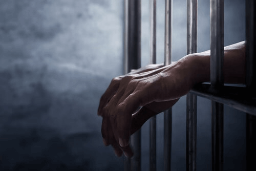 Les mains d'une personne ayant une liberté provisioire derrière des barreaux 
