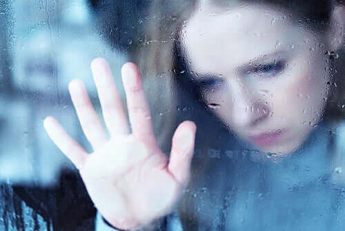 Une femme posant une main à la fenêtre triste à cause de l'anxiété