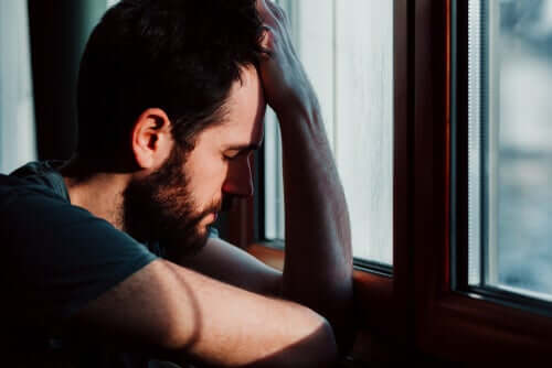 Un homme appuyé à la fenêtre envahi par l'anxiété