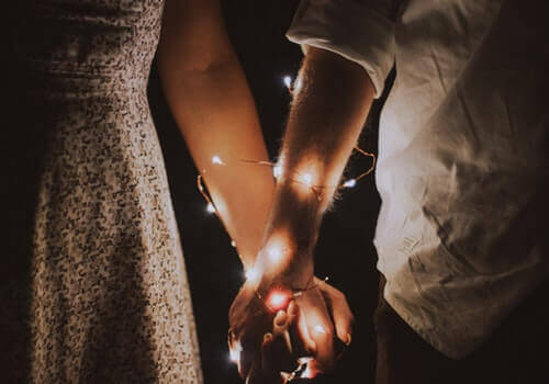 Deux personnes se tenant la main avec une guirlande lumineuse enroulée autour de leur bras