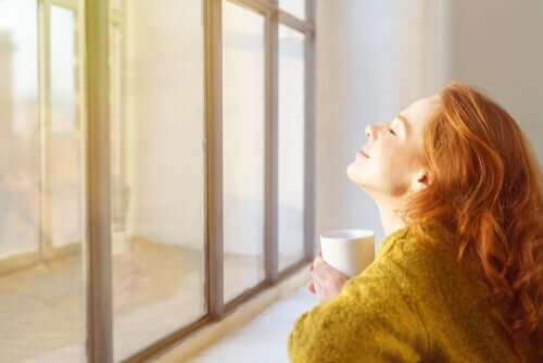 Une femme devant sa fenêtre buvant un café pendant le confinement