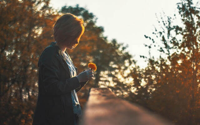 Une femme regarde par terre en tenant une fleur.