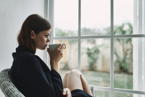 Une femme buvant dans une tasse face à une fenêtre pendant le confinement