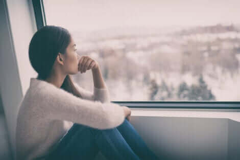 Une femme morose regardant le jour gris par la fenêtre.