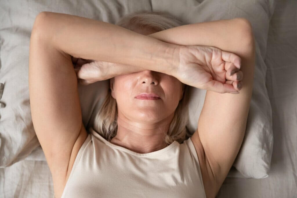 Une femme couchee sur son lit, les bras sur ses yeux. 