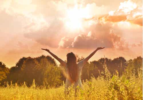 Une femme dans la nature qui lève les bras au ciel.