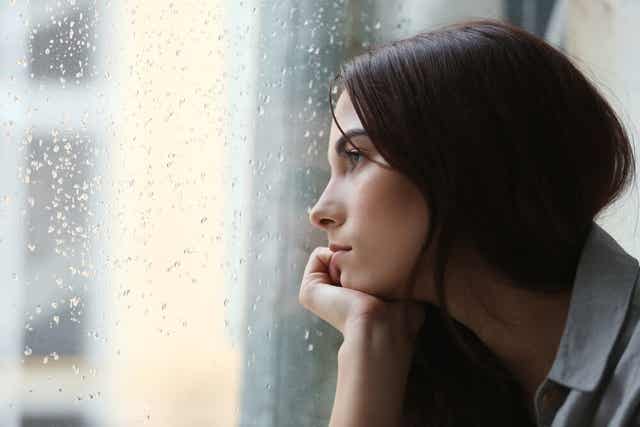 Femme qui regarde la pluie à travers la fenêtre.