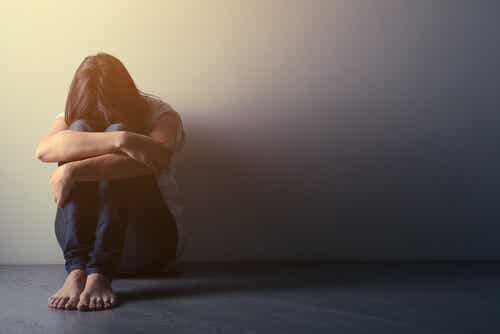 Une femme triste assise contre un mur.